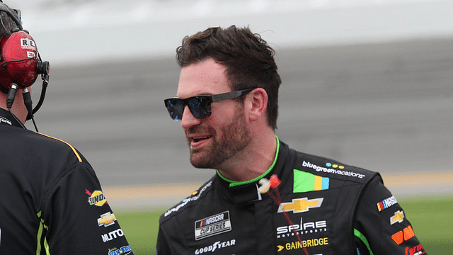 Corey LaJoie talks with crew members while he waits to qualify, Friday, February 16, 2024, for the Fresh From Florida 250 at Daytona International Speedway.