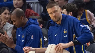 New Golden State Warriors forward Kristaps Porzingis (with towel) watches the action against the Boston Celtics from the bench during the first quarter at Chase Center